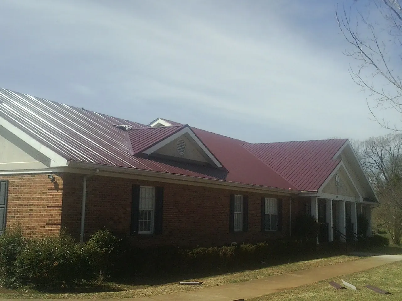 Red metal roof with gabled entries on a long brick building, from a Hail Damage Roof Repair job in Augusta